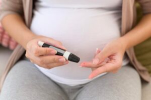 Pregnant woman checking blood sugar levels with a glucose meter, focusing on gestational diabetes management.